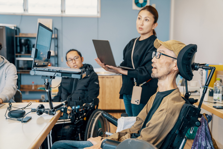 People with disabilities and colleagues gathered around assistive technology in a group setting